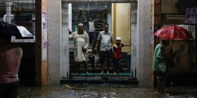 People wait on the gate of a mosque as streets are flooded before the Cyclone Sitrang hits in Dhaka