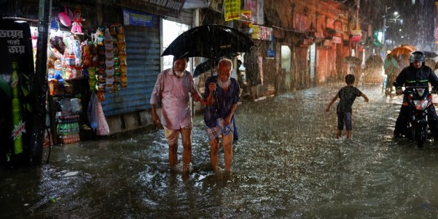 People wade through a flooded street amid continuous rain before the Cyclone Sitrang hits in Dhaka