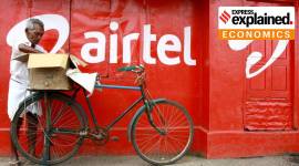 A man with a cycle stands against a wall painted with the airtel logo.