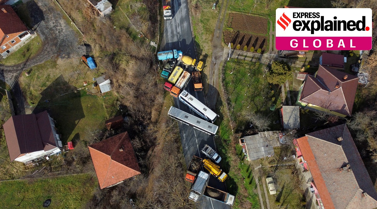 A bird's eye view of a roadblock with multiple buses and other big vehicles halting movement on a narrow road.
