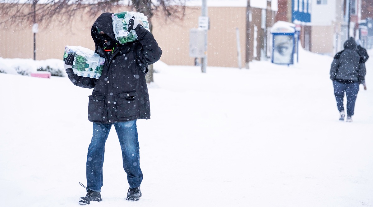 A pedestiran carries packs of bottled water along a snow covered street in Buffalo, New York, Dec. 26, 2022. Thousands remain without power in the Buffalo region, where there is as much as 49 inches of snow on the ground, with more still falling. (Brendan Bannon/The New York Times)
