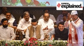 Abdul Sattar walks on a stage with folded hands after being sworn-in as a minister, as Deputy CM Devendra Fadnavis and CM Eknath Shinde are seated behind him.
