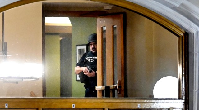 A police officer, with his gun drawn, is seen through the window at an entrance at the Michigan State University Union following shootings on campus on Feb. 13, 2023, in East Lansing, Michigan. (Nick King/Lansing State Journal via AP)
