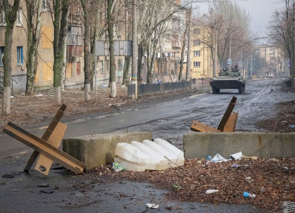 Ukrainian service members ride a BMP-2 infantry fighting vehicle along an empty street.