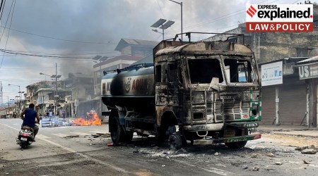 A scooterist rides past a damaged water tanker that was set afire during a protest by tribal groups in Churachandpur