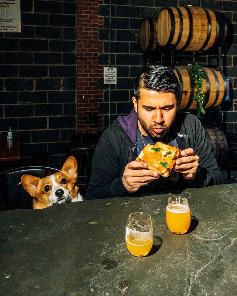 A customer is joined by his dog as he eats a pizza at a Traze pop-up inside Fifth Hammer Brewing in Queens, April 26, 2023. (DeSean McClinton-Holland/The New York Times)