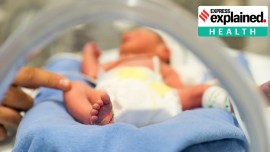 Photo of a premature baby in incubator. Focus is on his feet and toes. The doctor is touching him to check his reflexes. There are cables and tubes in the out-of-focus area.