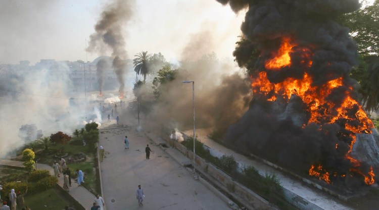 Smoke erupts from a burning objects set on fire by angry supporters of Pakistan's former Prime Minister Imran Khan as police fire tear gas to disperse them during a protest against the arrest of Khan, in Peshawar, Pakistan, May 9, 2023. (AP)