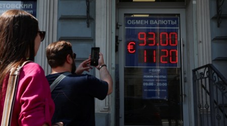 A man takes photos of a board showing currency exchange rates of the Euro against the Russian rouble in Saint Petersburg