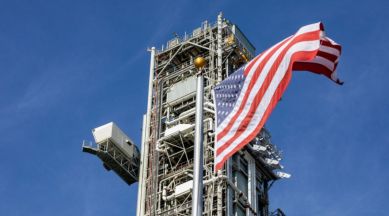 An American flag in the foreground with the mobile launcher for the artemis 2 mission in the background