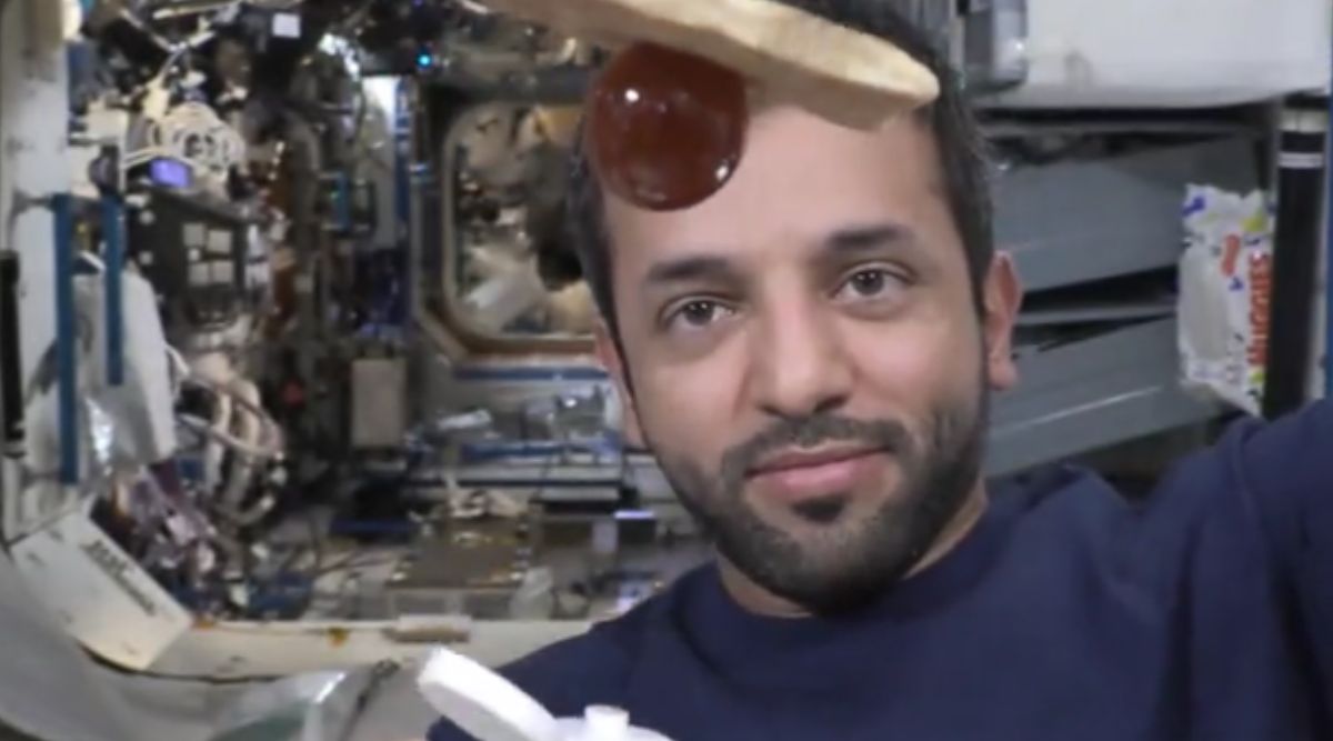 A blob of honey attached to a piece of bread on the international space station. An astronaut's face is in the background