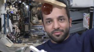 A blob of honey attached to a piece of bread on the international space station. An astronaut's face is in the background