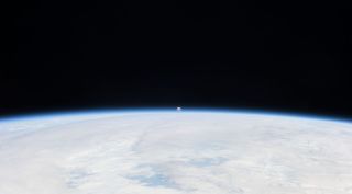The Moon can be seen in the distance with the Earth in the foreground.