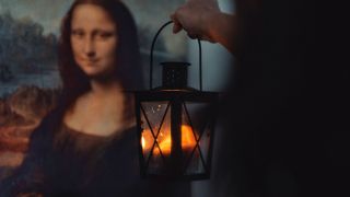A person holding a lamp in front of a copy of the mona lisa