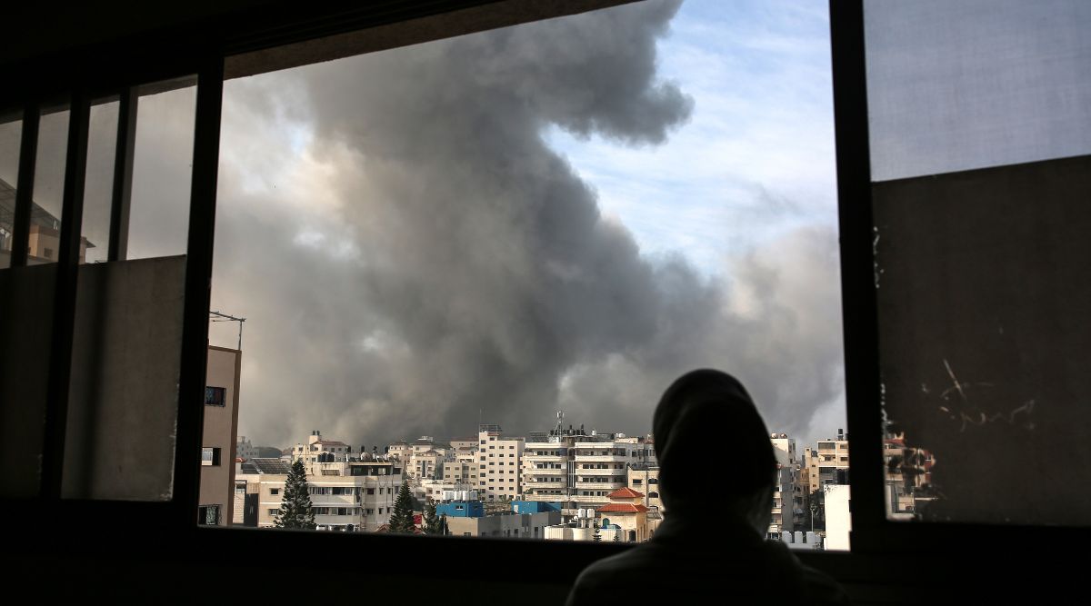 A woman watches from an apartment in Gaza City as smoke rises from Israeli airstrikes on Wednesday, Oct. 11, 2023. Israel heavily bombarded targets in Gaza for a fifth day on Wednesday a