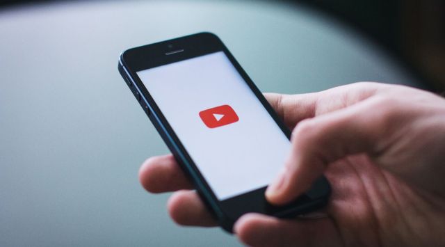 A man holding a smartphone displaying the YouTube logo on a white background