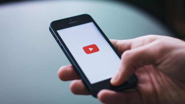 A man holding a phone with a YouTube logo displayed.