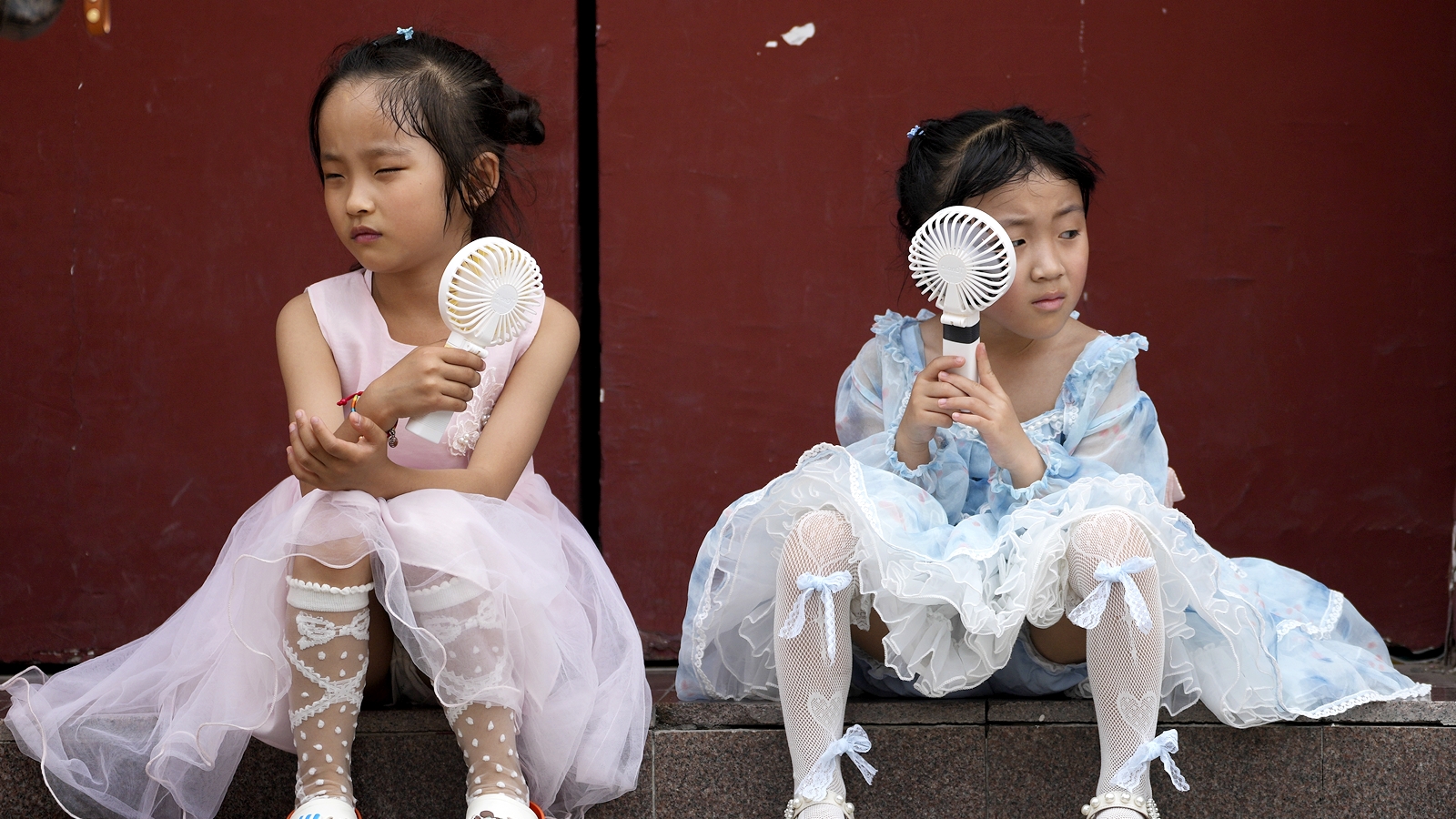 Children cool themselves with electric fans as they take a rest near the Forbidden City on a hot day in Beijing, June 25, 2023. (AP Photo/Andy Wong)
