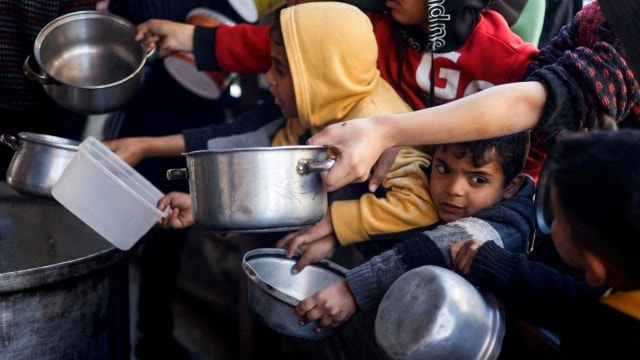 FILE PHOTO: Palestinian children wait to receive food cooked by a charity kitchen amid shortages of food supplies, in Rafah