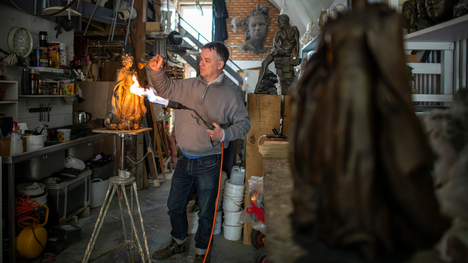 The sculptor Hywel Pratley uses ferric nitrate and a torch flame to add a patina to a limited edition maquette of his Queen Elizabeth II statue, at his studio in London, April 16, 2024. (Joshua Bright/The New York Times)