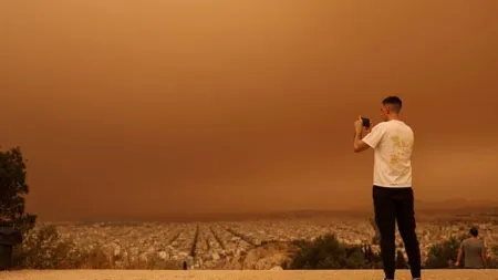 A man takes pictures as African dust from the desert of Sahara covers the city of Athens, Greece