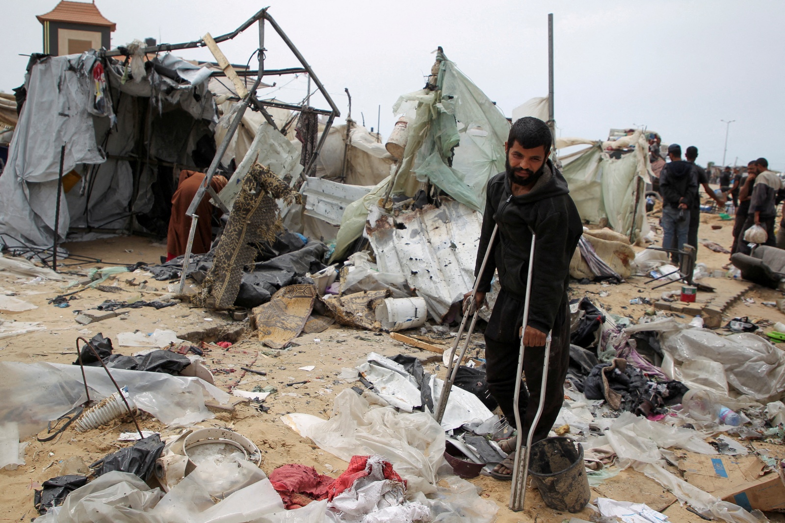 A man looks on as Palestinians inspect a tent camp damaged in an Israeli strike during an Israeli military operation, in Rafah, in the southern Gaza Strip, May 28, 2024. REUTERS