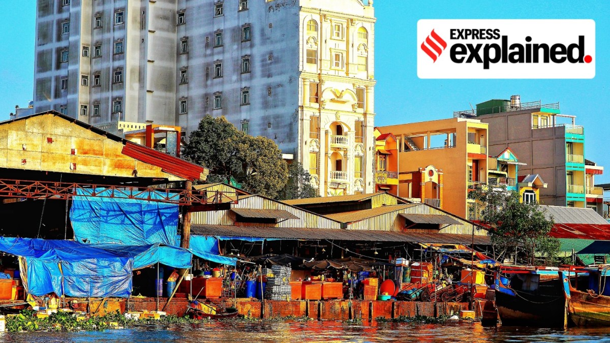 Riverbank with slums in the foreground and high-rise building in the background.