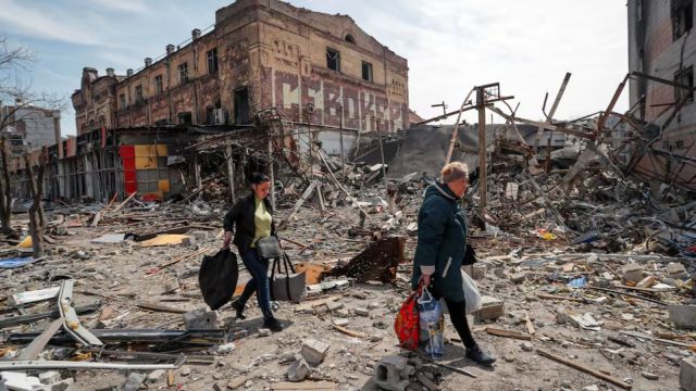 Residents carry their belongings near buildings destroyed in the course of Ukraine-Russia conflict, in the southern port city of Mariupol, Ukraine (Reuters)