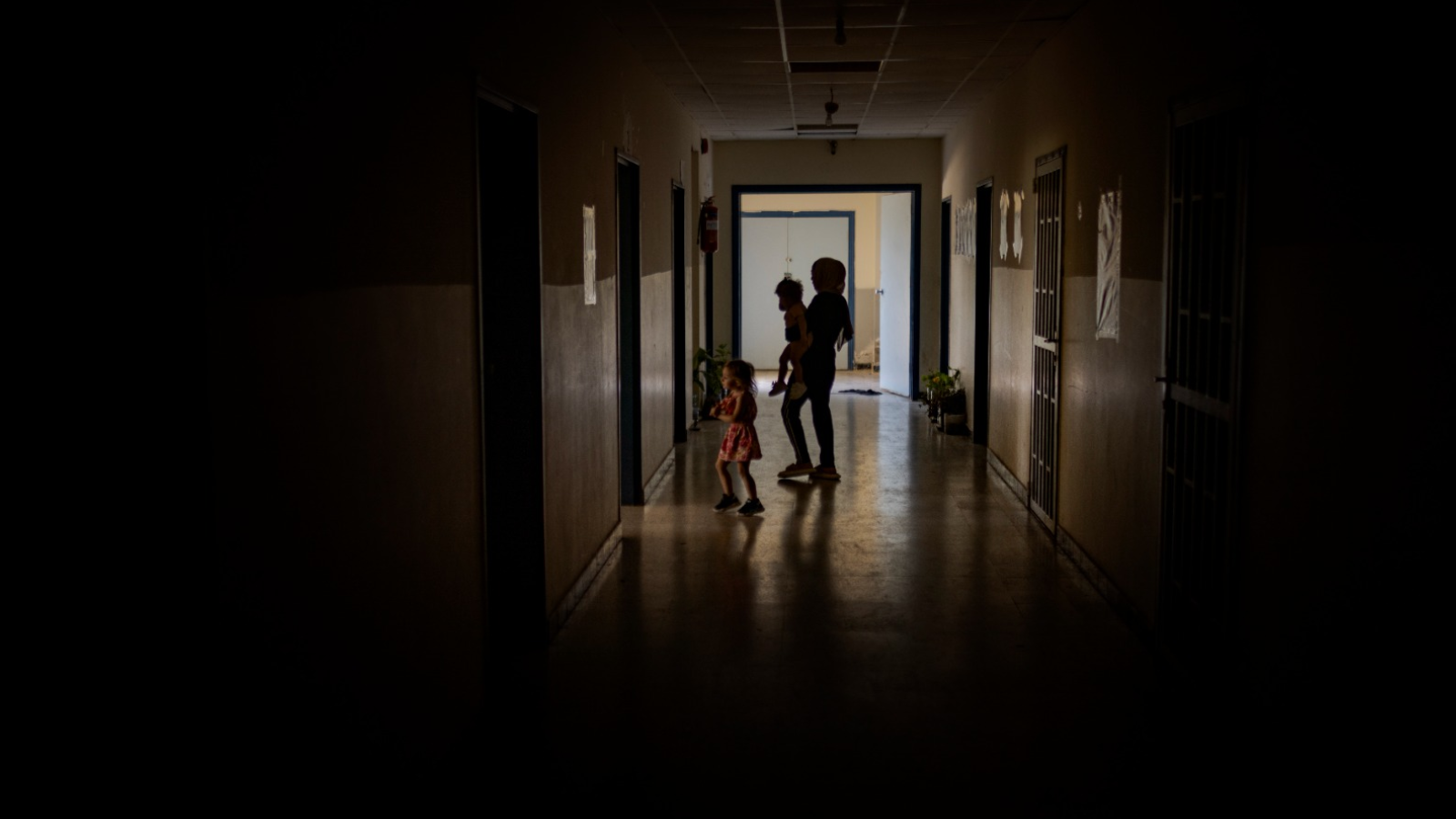 A family in a dark corridor at a school housing people displaced along Lebanon's southern border with Israel amid rising tensions between Hezbollah and Israel, in Tyre, Lebanon, May 20, 2024. Israel and Hezbollah have their reasons for calibrating their attacks to avoid a regional conflict.  (photo: New York Times)