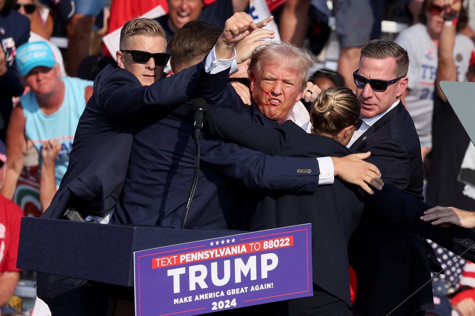 Republican presidential candidate and former U.S. President Donald Trump gestures with a bloodied face while he is assisted by U.S. Secret Service personnel after he was shot in the right ear during a campaign rally at the Butler Farm Show in Butler, Pennsylvania, U.S., July 13, 2024. REUTERS/Brendan McDermid