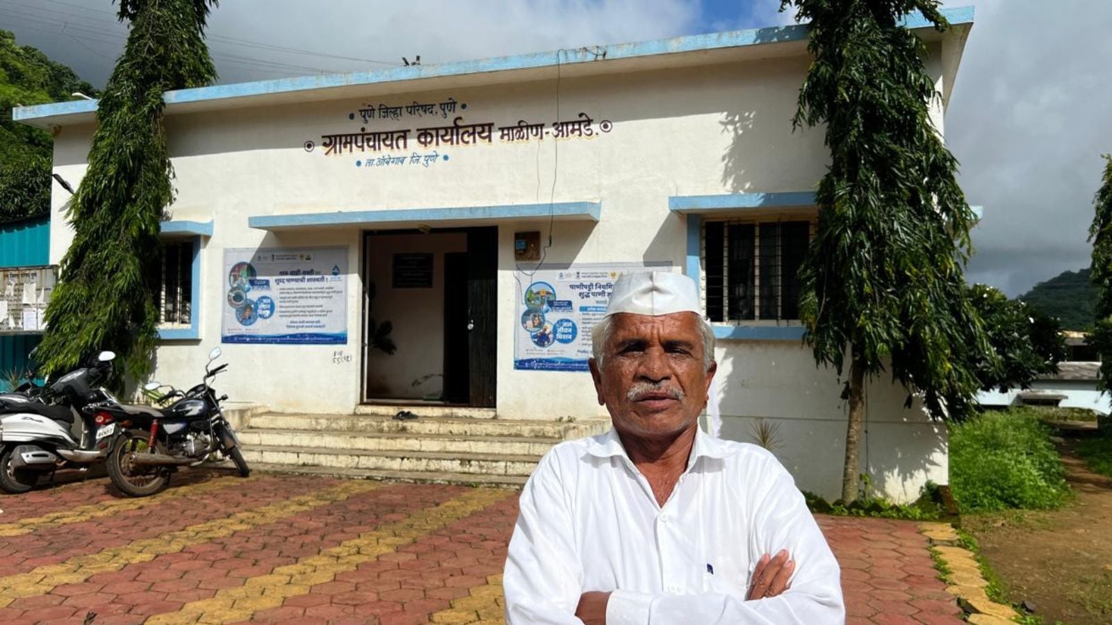 Malin Sarpanch Raghunath Zhanzare in front of the Gram Panchayat office built as part of the village rehabilitation. Express Photo by Pavan Khengre
