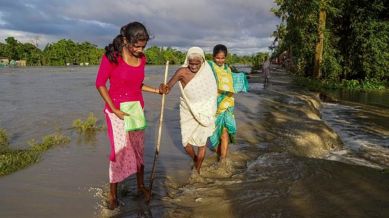 An elderly woman being assisted to cross a waterlogged street, in Morigaon