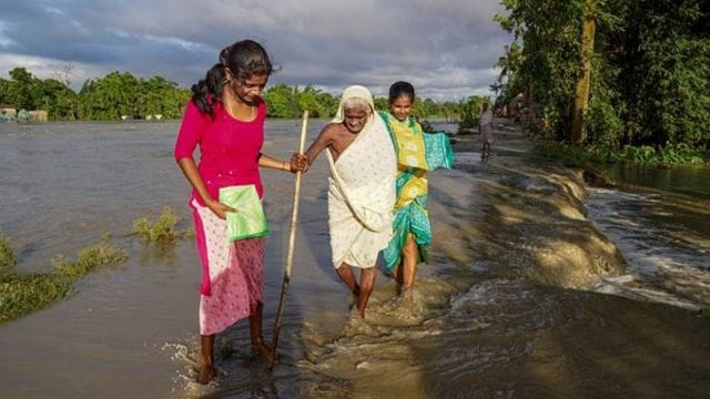 An elderly woman being assisted to cross a waterlogged street, in Morigaon