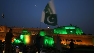 A Pakistani waves national flag in front of the 'Bala Hissar' which is illuminated with the national flag colors during the 78th Pakistan Independence Day celebrations, in Peshawar, Pakistan, Tuesday, Aug. 13, 2024. (AP Photo/Muhammad Sajjad)