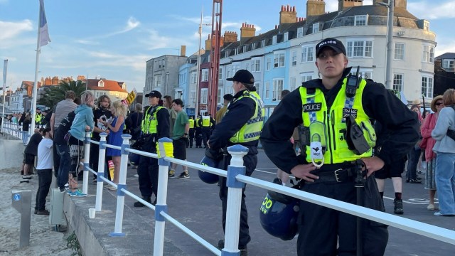 Police warring riot protection equipment patrol the seafront esplanade following an anti immigration protest in Weymouth