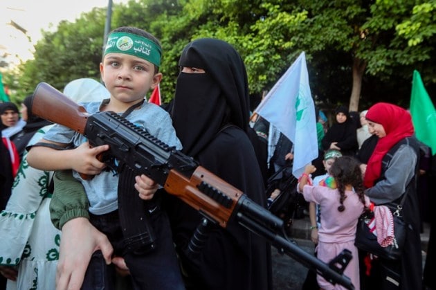 A supporter of the Islamist Hamas movement carries her son, who holds a machine gun toy during a protest in the southern port city of Sidon, Lebanon, Wednesday, July 31, 2024, to condemn the killing of Hamas political chief Ismail Haniyeh.