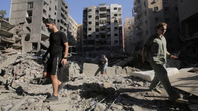 People walk on the rubble at the site of the Israeli airstrike that killed Lebanon's Hezbollah leader Sayyed Hassan Nasrallah on Friday, in Beirut's southern suburbs