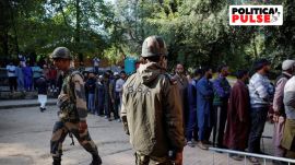 Indian security personnel stand guard outside a polling station, as people queue to vote at a polling station, during the first phase of assembly election, in south Kashmir's Kokernag