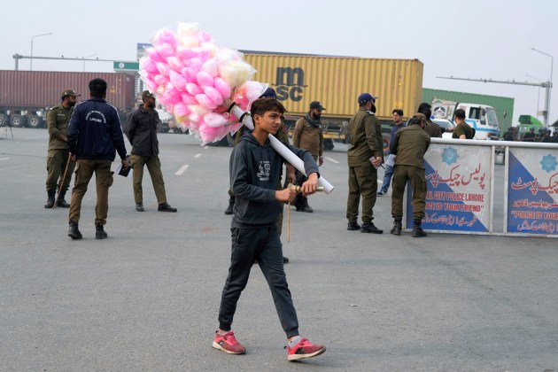 A cotton-candy seller walks past police officers stand guard on an entry point to motorway leading to Islamabad, which has been closed by authorities due to a planned rally by supporters of imprisoned former Prime Minister Imran Khan's Pakistan Tehreek-e-Insaf party, in Lahore, Pakistan, Saturday, Nov. 23, 2024. (AP Photo/K.M. Chaudary)