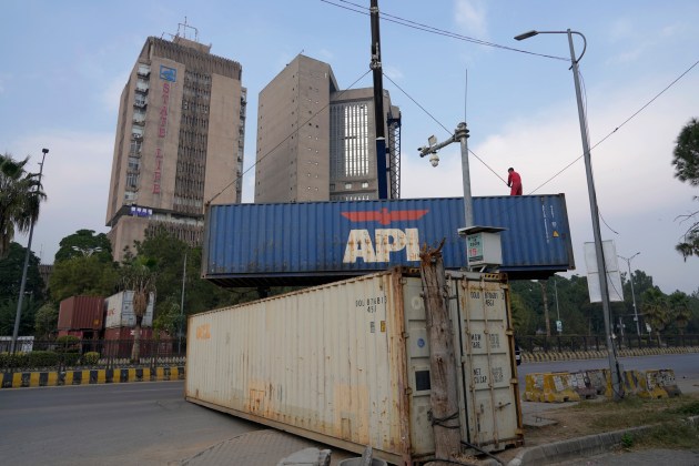 A worker places shipping containers to close a road ahead of a planned rally by supporters of imprisoned former Prime Minister Imran Khan's Pakistan Tehreek-e-Insaf party, in Islamabad, Pakistan, Saturday, Nov. 23, 2024. (AP Photo/Anjum Naveed)