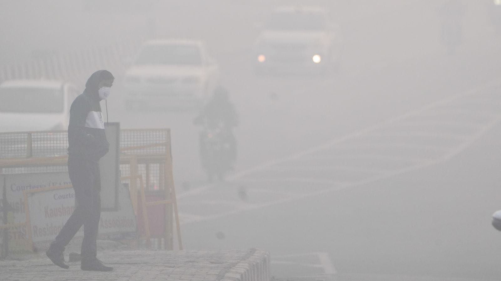 A man crosses a road amid dense fog in New Delhi,