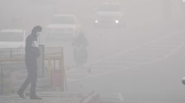 A man crosses a road amid dense fog in New Delhi,