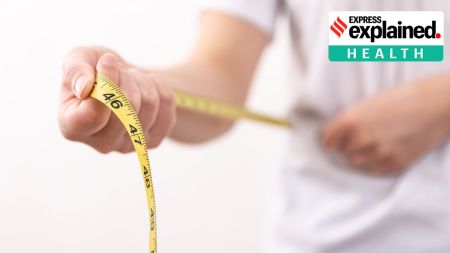 A woman in a white tshirt holds a yellow centimeter tape in her hands; Obesity, Lancet definition