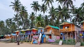 Beach shacks visible with coloured exteriors and palm trees on a goa beach