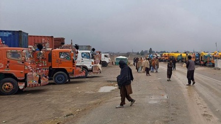 People move past parked trucks loaded with supplies at the Torkham border crossing following the closure of the border crossing between Pakistan and Afghanistan