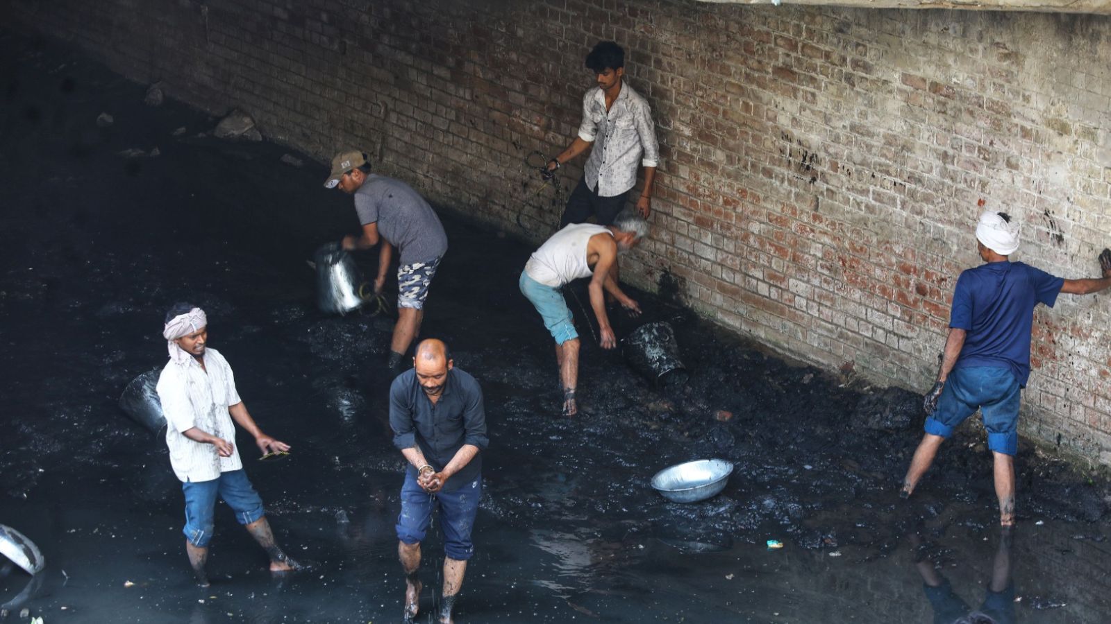 Carrying steel buckets and pans in their hands, the men waded into ankle-deep black muck to clean the drain, which falls under the Irrigation and Flood Control Department.