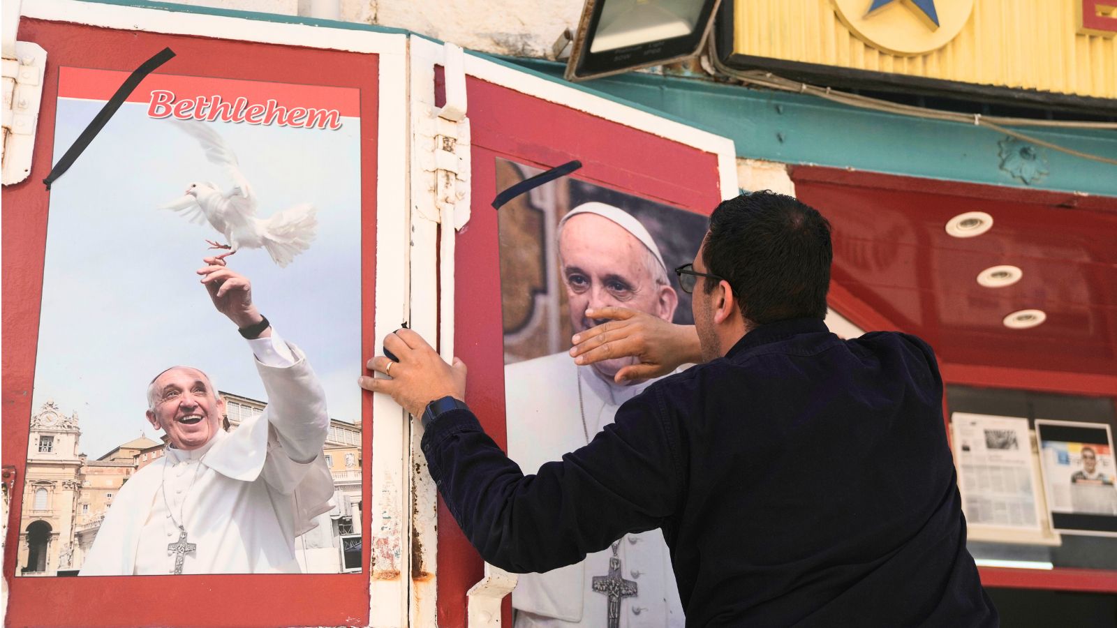 A shop owner cleans and places a black ribbon over a photo of the late Pope Francis after the news of his death at age 88, in Bethlehem, West Bank