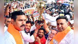 BJP President BY Vijayendra with party workers, who are wearing face masks with pictures of Siddaramaiah and Shivakumar and carrying a replica of the IPL trophy as they protest against the state government over the Bengaluru stampede. (ANI Photo)