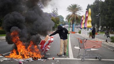 A protester places debris in a fire as Border Patrol personnel in riot gear and gas masks stand guard outside an industrial park in Paramount, Calif., on Saturday, June 7, 2025. (AP Photo/Eric Thayer)