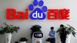 Men interact with a Baidu AI robot near the company logo at its headquarters in Beijing, China April 23, 2021. (File Image: Reuters/Florence Lo)